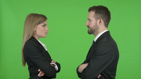 Young Male and Female Professionals Standing and Staring at Each Other Against Chroma Key