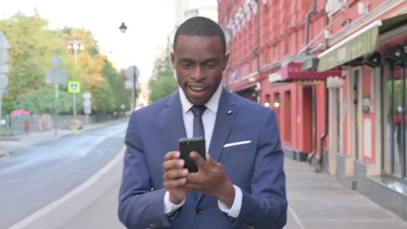 African Businessman Having Success on Smartphone While Walking on Street