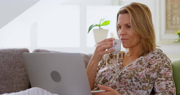 Woman having coffee while using laptop on sofa 4k