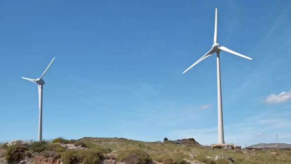 Diagonal Shot of Two Wind Turbines and Road In-between in Hill Landscape on Sunny Day