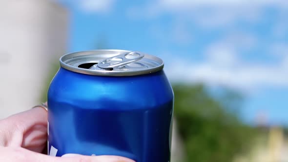 Female Hand Stretches an Open Tin Beer Can Up on a Blurred Backdrop of Nature