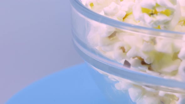 Bowl of popcorn rotating over a blue surface, macro shot in 4k.