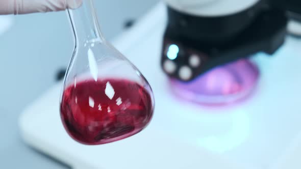 Scientist Mixing Pink Liquid in the Glass Flasks