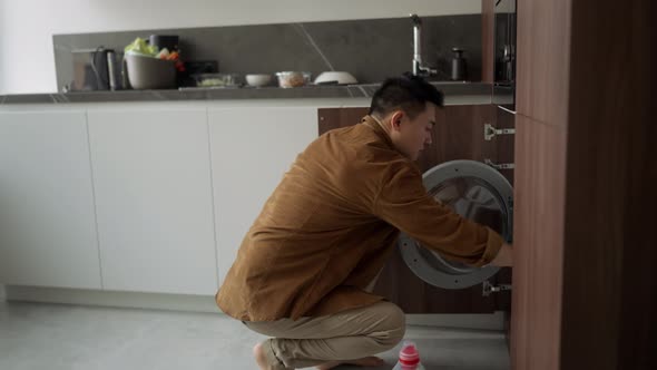 Serious Asian man wearing casual cloth turns on washing machine