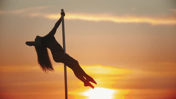 Young Woman Holding By the Dancing Pole and Showing Movements on Sunset