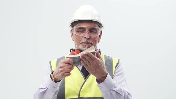 Adult Man Engineer Holds and Counts a Stack of Dollar Bills Looking Into the Camera in the Studio on