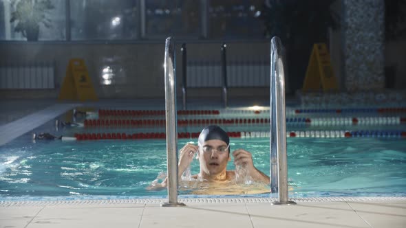 Swimming Sports  Young Man Swimmer Comes Up From the Pool Using the Ladder and Looks in the Camera