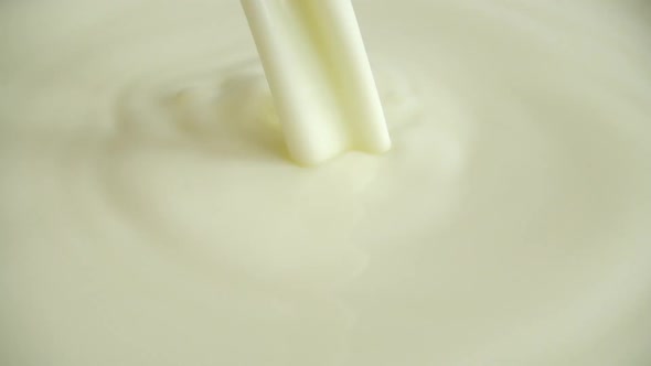 A pouring stream of milk into the milky surface. Slow motion.