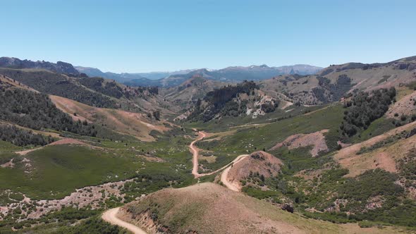 Aerial view of a winding dirt road through the mountains. Droneing backwards and descending.