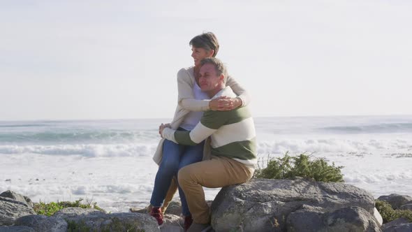 Caucasian couple enjoying free time by sea on sunny day sitting and embracing