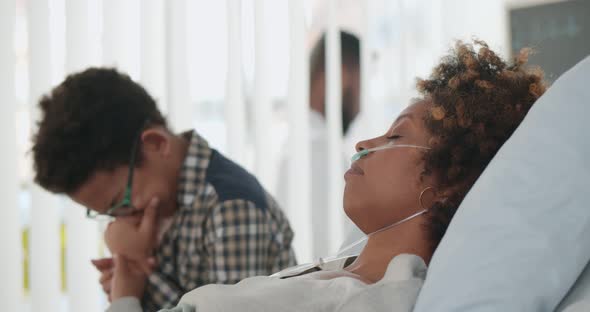 Preteen Afroamerican Boy Sitting in Hospital Ward and Crying Holding Hand of Ill Mother