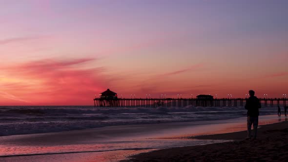 A man enjoys his vacation at the beach during a gorgeous red, purple, tangerine, pink and blue sunse