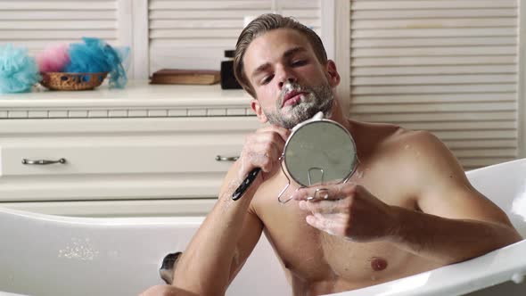 Young Man Shaving Face Near Mirror in Bathroom. Male Beauty, Beard Care Skincare Concept
