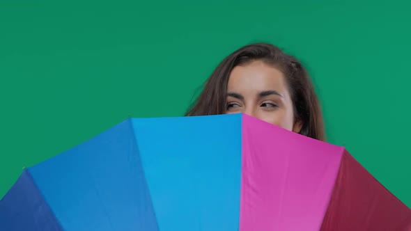 Cute Young Woman Looking Through Multicolored Umbrella on Green Screen, Chroma Key.