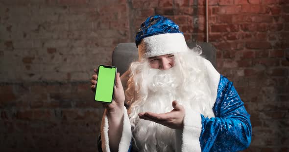 Santa Claus in Blue Costume Shows Mobile Phone with Green Screen in His Hand