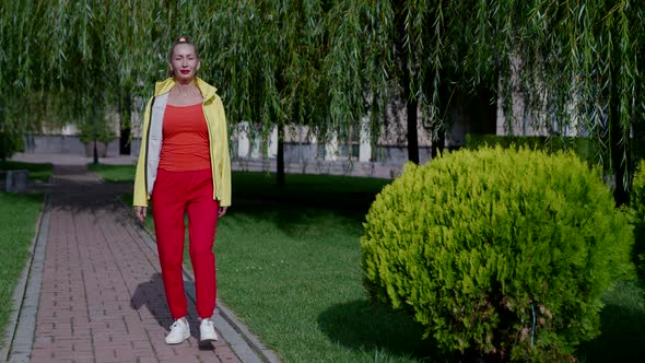 a Woman in Red Clothes and a Yellow Jacket Walks in a City Park