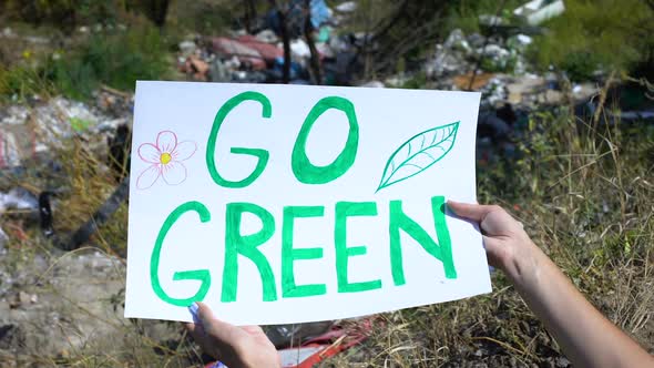 Go Green Phrase on Cardboard in Person Hands Against Open Dumping Background