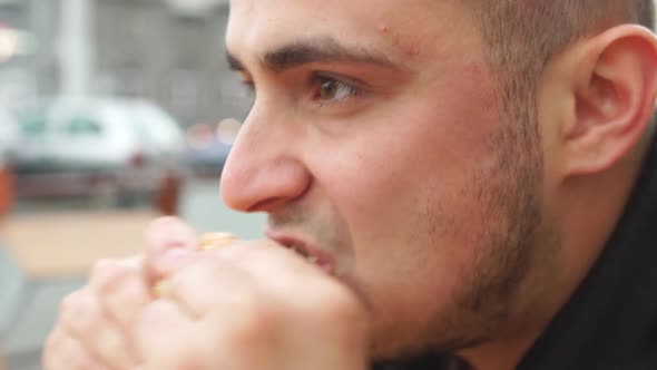 Close up of young man eating tasty burger in street food cafe