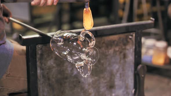 Glassblower adding molten glass to vase. Handheld, shallow focus