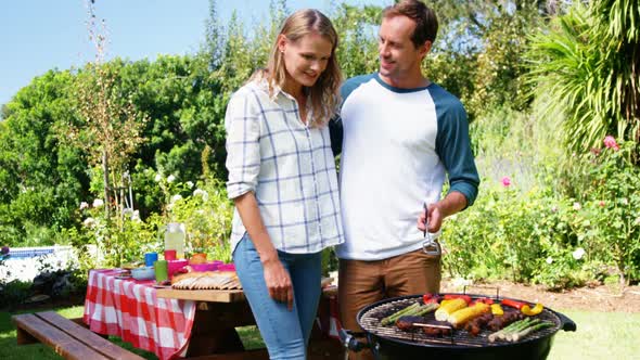 Couple grilling meat and vegetables on barbecue