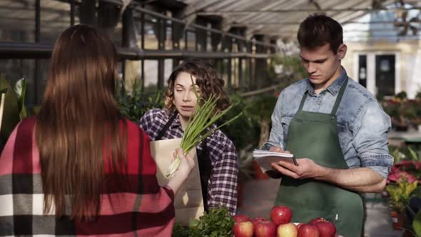 European Saleswoman Wearing Apron is Giving Organic Food to Customer in Greenhouse