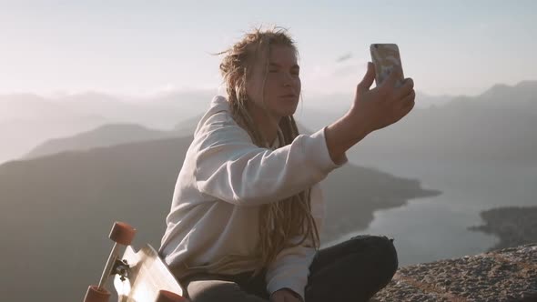 Happy dreadlocks woman longboarder making selfie photos with smartphone against mountain