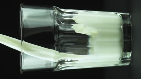 Vertical Video Milk Pouring Into Faceted Glass Close Up Isolated on Black Background Slow Motion