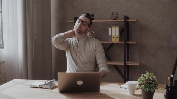 a Man Has a Sore Neck After Hard Work at a Table with a Laptop. Pain in the Neck