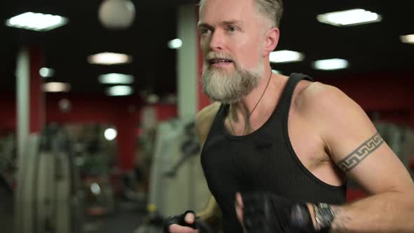 Adult gray-haired man running on a treadmill in a gym