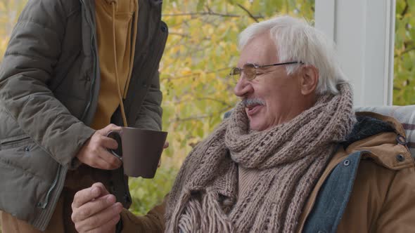 Child Bringing Tea Cup to Grandfather Sitting on Terrace