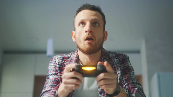 A Excited Young Gamer is Sitting on a Couch and Playing Video Games on a Console