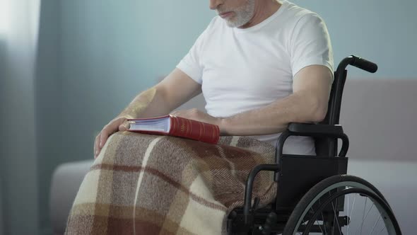 Old age man with disabilities reviewing album with photos, missing relatives