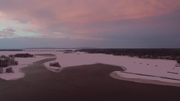 Beautiful sunset skies seen by drone flying forward over half frozen lake