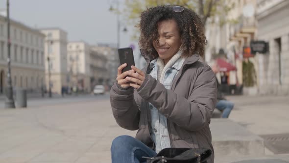 Beautiful Girl with Afro Haircut Sitting on Bench at City Street