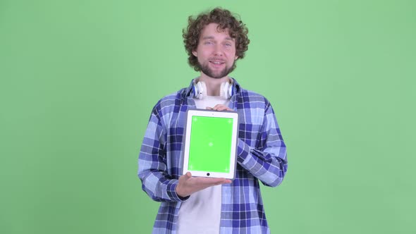 Happy Young Bearded Hipster Man Talking While Showing Digital Tablet