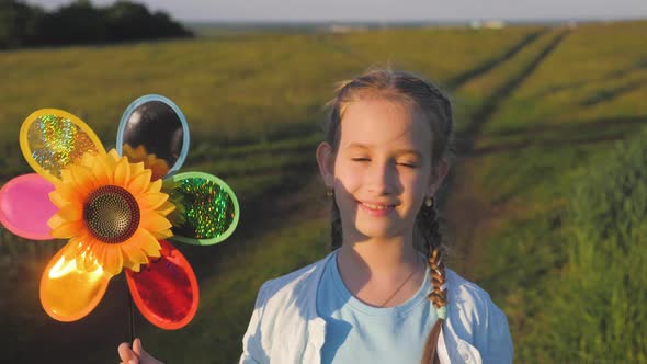 Happy Girl Holding Wind Toy in Green Field, Rejoicing Life. Cheerful Child in the Meadow with Wind