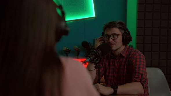 Young man talking in mic while recording podcast with crop coworker