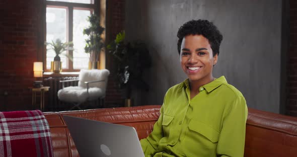 Beautiful African American Young Woman Looking at Camera Smiling Sitting on Couch Used Laptop