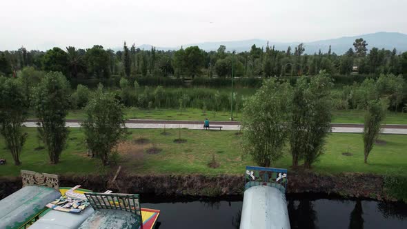 Dolly out with jib up above a lake and natural area with view of a trail and a runner resting, in Xo