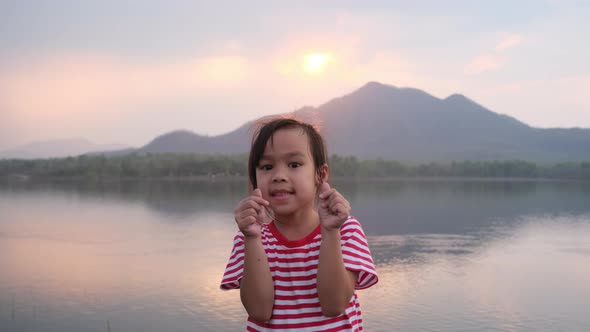 Smiling cute little girl doing mini heart gesture with her hands and looking. alt