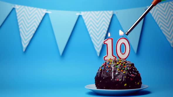 chocolate birthday cake with a burning candle number ten, 10 on a blue background. Copy space. place alt