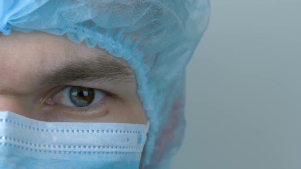 Young male doctor in protective medical face mask, close up. Half face wearing mask and cap