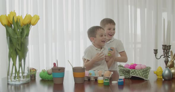 Two Little Brothers are Smiling Tickling Each Other While Painting Easter Eggs