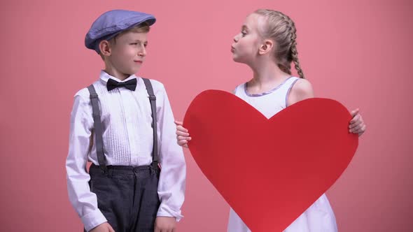 Little Girl With Red Paper Heart Trying to Kiss Young Boy Male Kid Recoils, Date