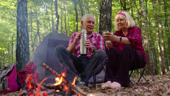 Senior Elderly Grandmother Grandfather Pouring Drink From Thermos Drinking Tea Over Campfire in Wood