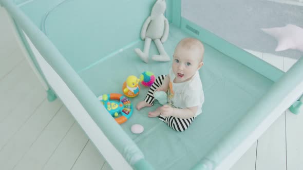 Cute Baby Girl Playing Toys in Playpen at Home