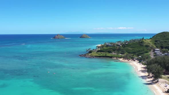 Drone flying over the tropical blue water of Oahu Hawaii towards the mokes island of Lanikai.