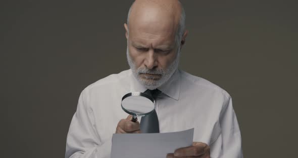 Businessman checking a document using a magnifier, contracts and agreements concept