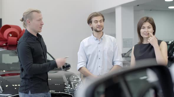 Confident Caucasian Man Presenting New Car To Couple in Dealership. Portrait of Successful Caucasian