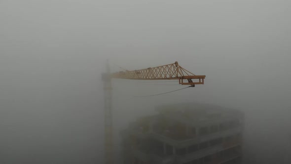 Birds eye view on tower crane boom in fog standing next to residential building.